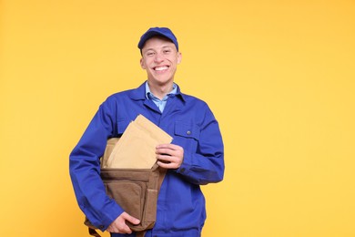 Happy postman with bag and envelopes on yellow background. Space for text