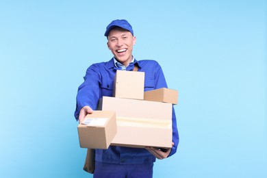 Happy postman giving parcels on light blue background