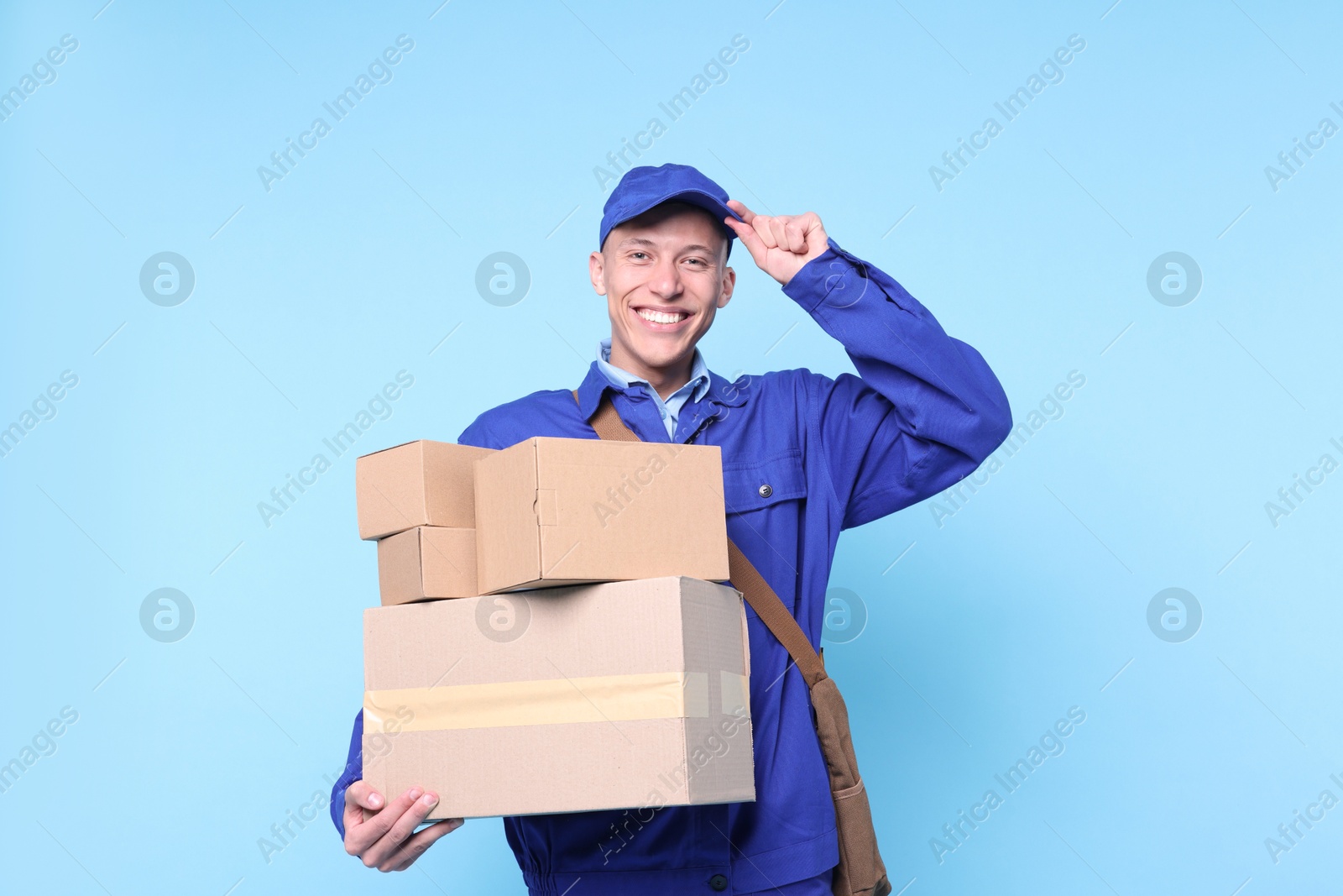 Photo of Happy postman with parcels on light blue background