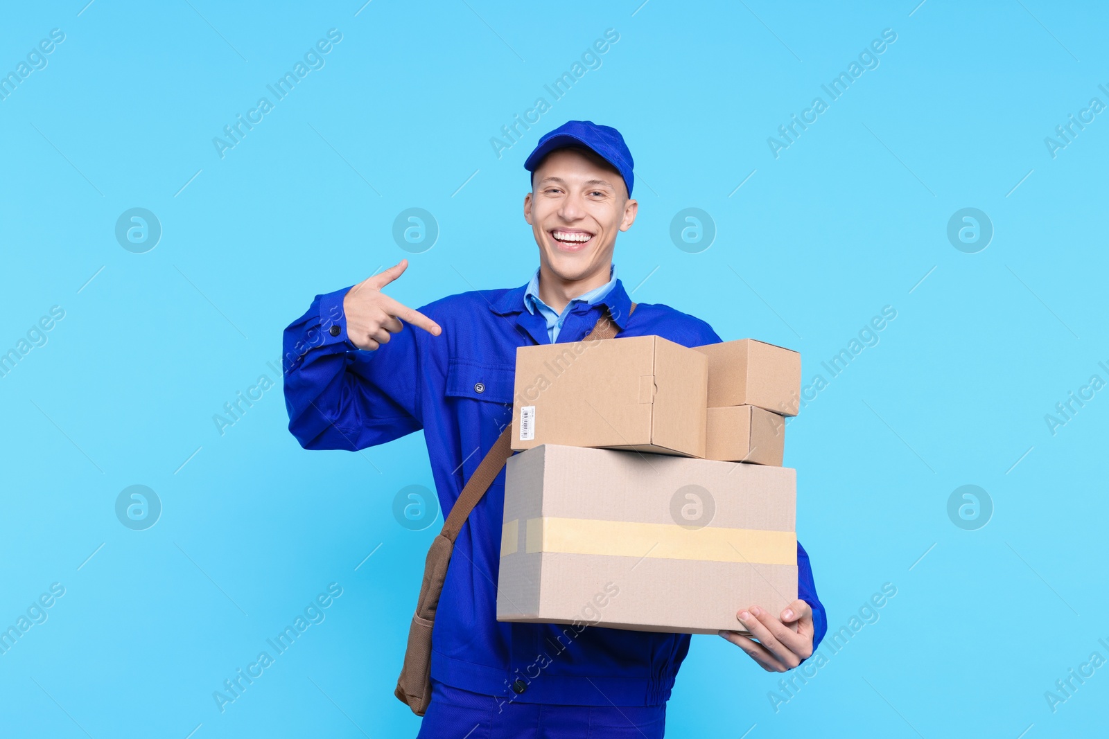 Photo of Happy postman pointing at parcels on light blue background