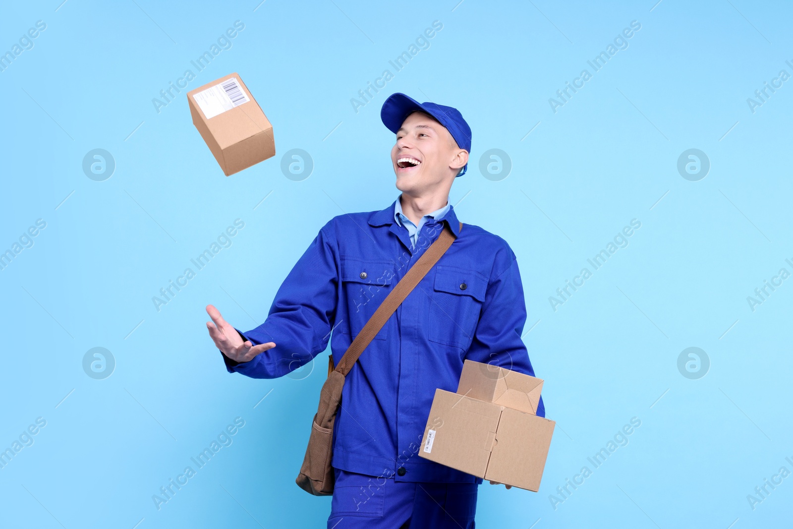 Photo of Happy postman with parcels on light blue background