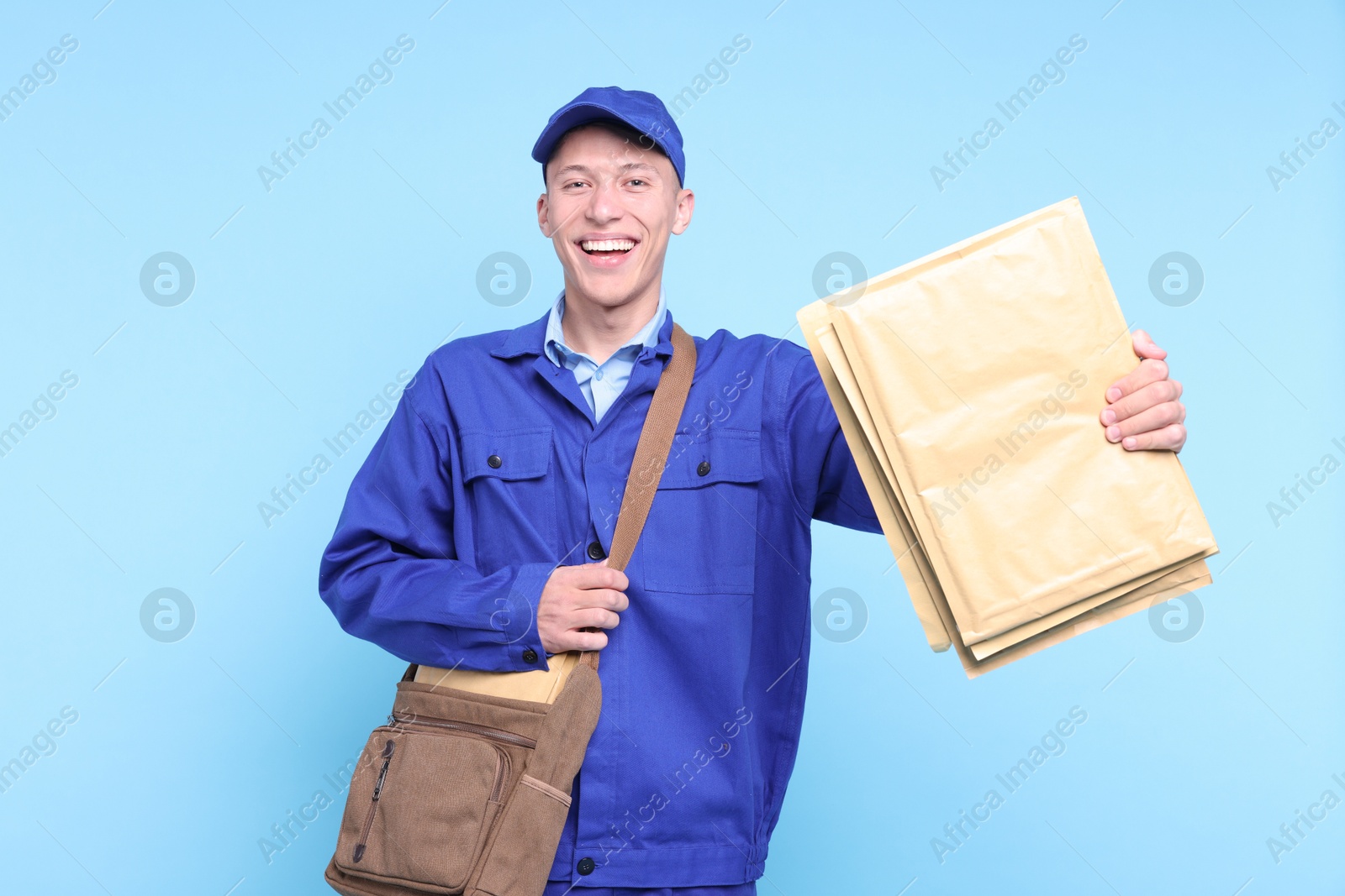 Photo of Happy postman with bag giving envelopes on light blue background