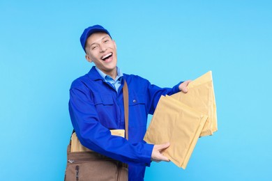 Photo of Happy postman with bag and envelopes on light blue background