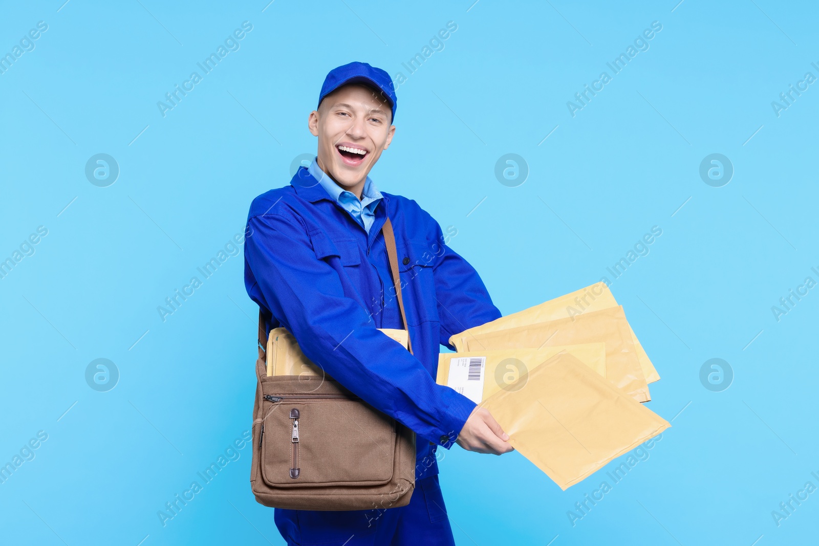 Photo of Happy postman with bag and envelopes on light blue background