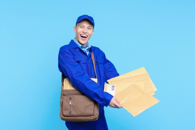 Happy postman with bag and envelopes on light blue background