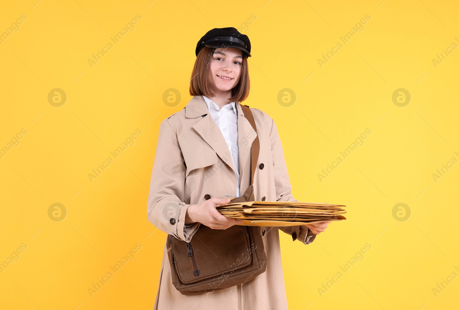 Photo of Happy postwoman with bag and envelopes on yellow background