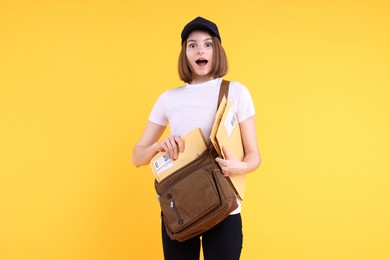 Photo of Emotional postwoman with bag and envelopes on yellow background