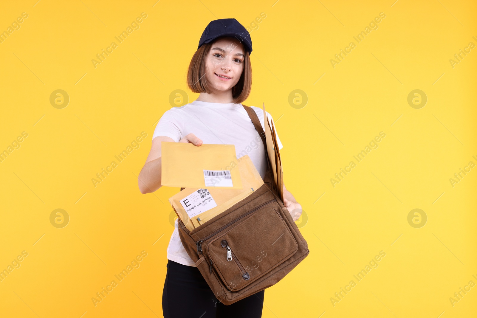 Photo of Happy postwoman with bag giving envelope on yellow background