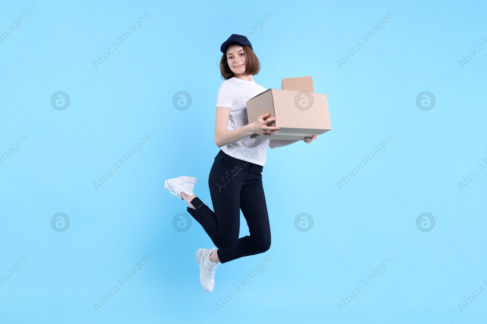 Photo of Happy postwoman with parcel jumping on light blue background