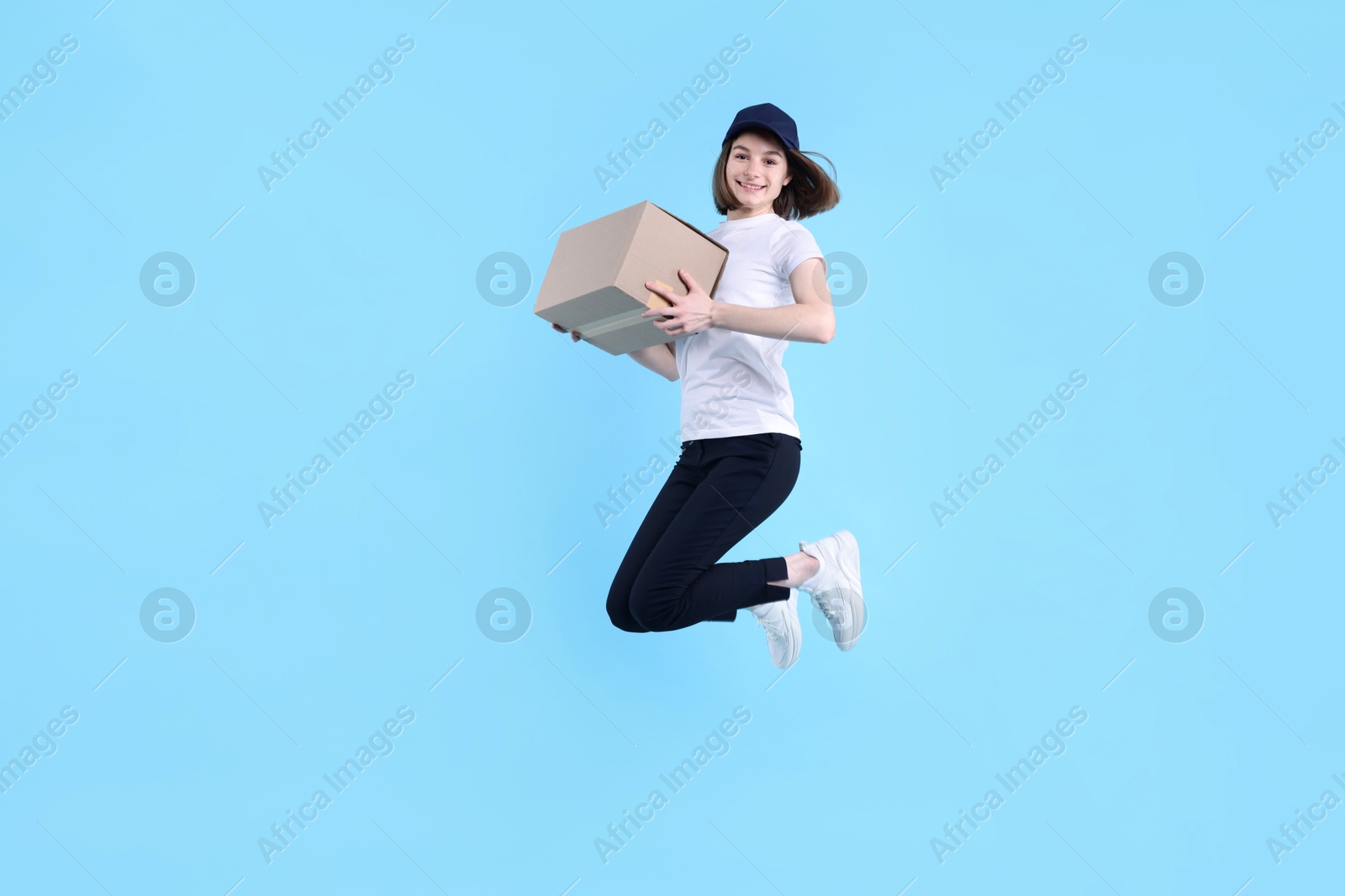 Photo of Happy postwoman with parcel jumping on light blue background