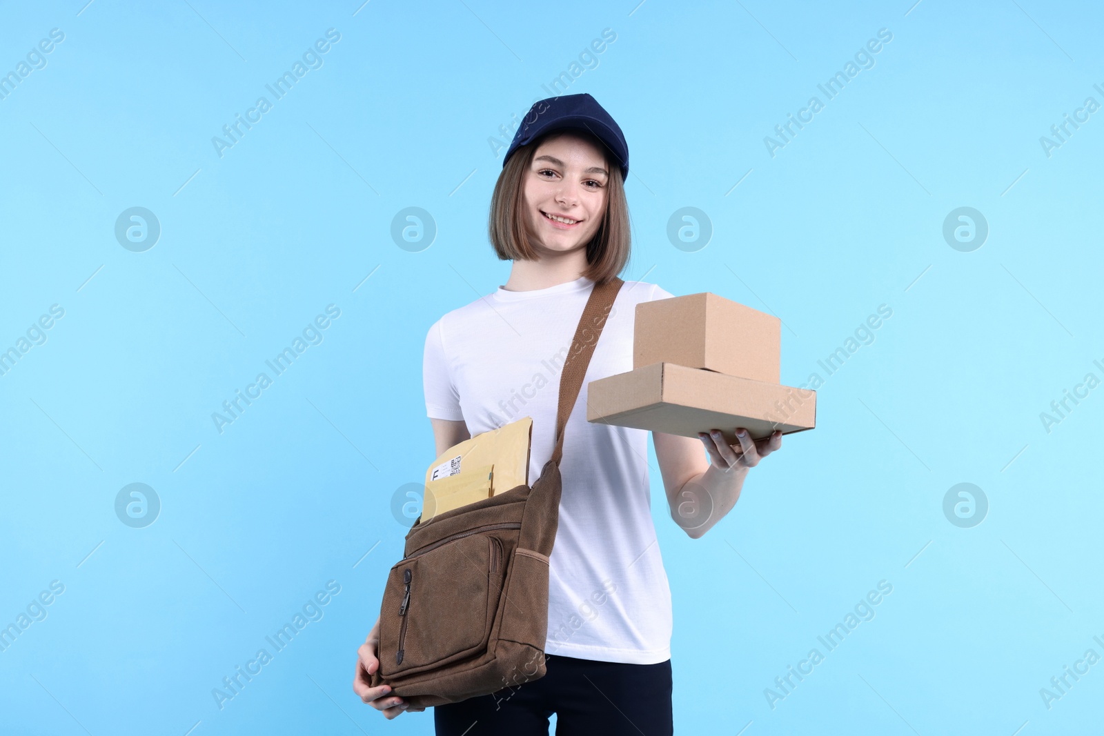 Photo of Happy postwoman with bag and parcels on light blue background