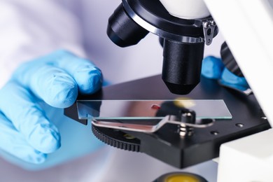 Photo of Scientist examining sample on slide under microscope, closeup