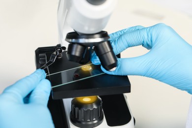 Photo of Scientist examining sample on slide under microscope, closeup