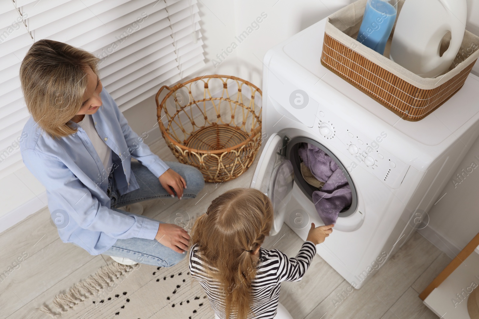 Photo of Little girl helping her mom doing laundry at home, above view