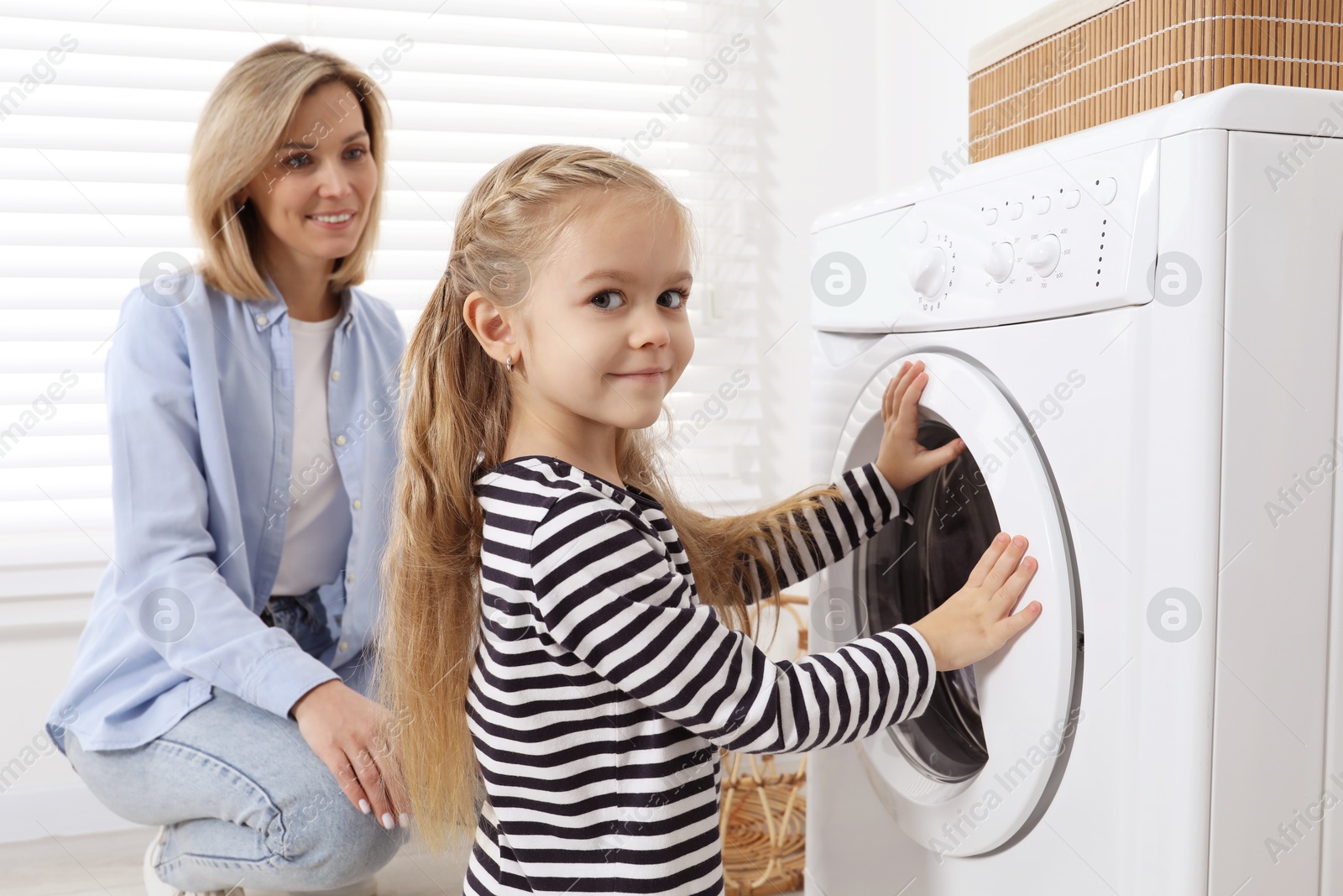 Photo of Little girl helping her mom doing laundry at home