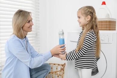 Photo of Little girl with detergent helping her mom doing laundry at home