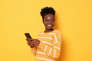 Happy woman with smartphone on yellow background