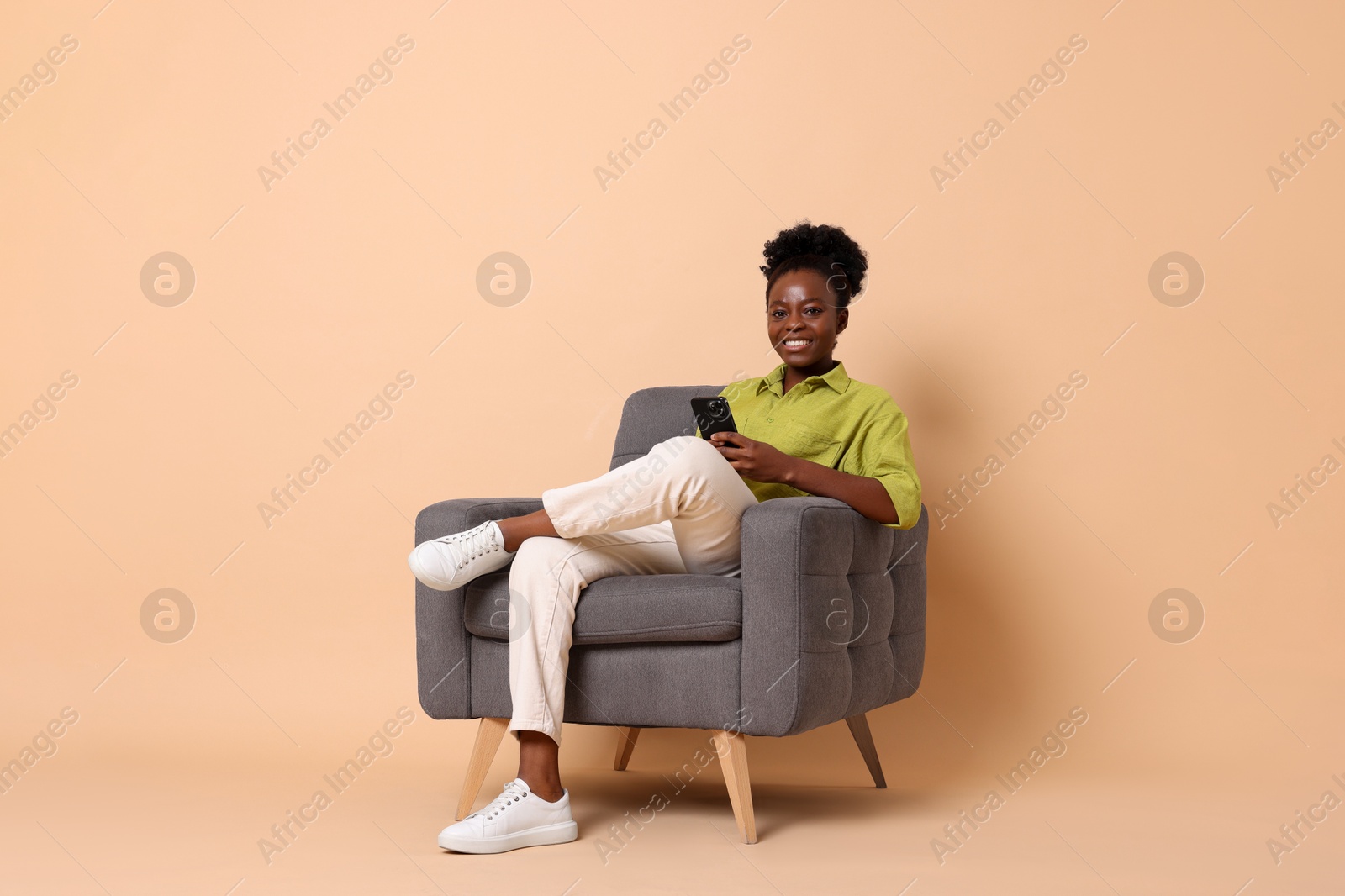 Photo of Smiling woman with smartphone sitting in armchair on beige background. Space for text