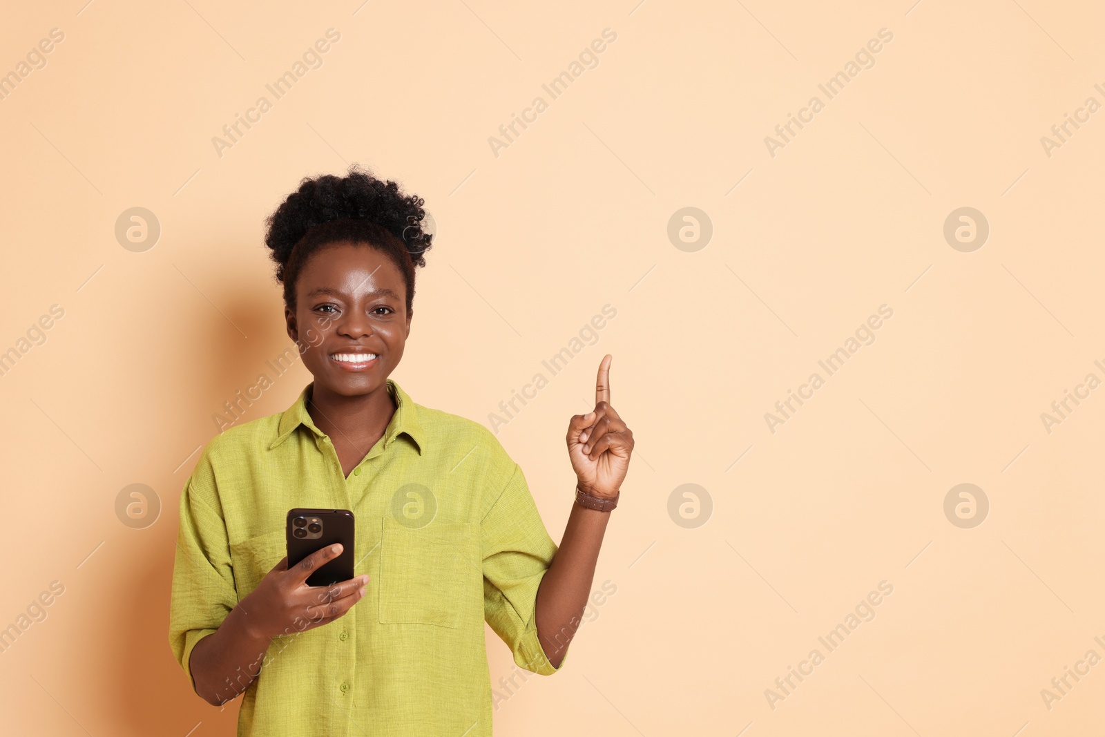 Photo of Cheerful woman with smartphone pointing at something on beige background. Space for text