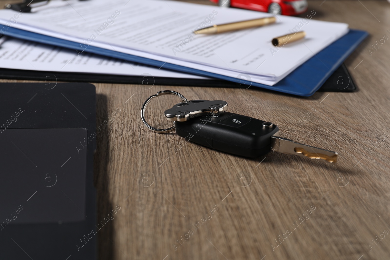 Photo of Car key and purchase agreement on wooden table, closeup. Buying auto