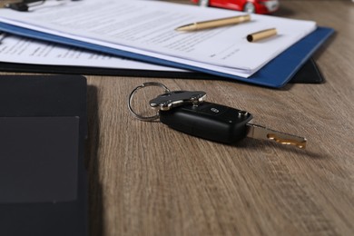 Car key and purchase agreement on wooden table, closeup. Buying auto