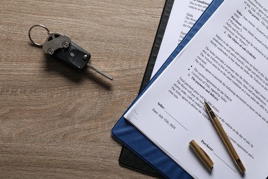 Photo of Car key and purchase agreement on wooden table, flat lay. Buying auto