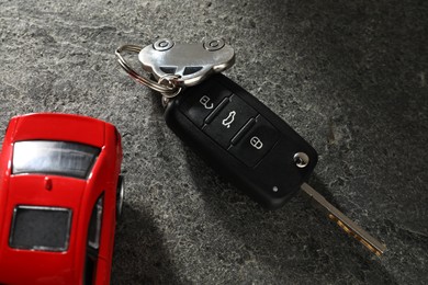 Car key and model on grey textured table, closeup. Buying auto