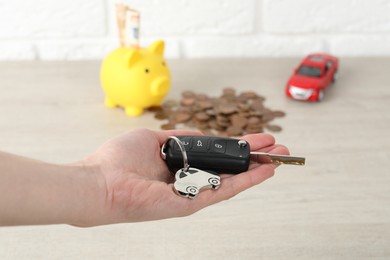 Photo of Woman with car key at light wooden table, closeup. Buying auto