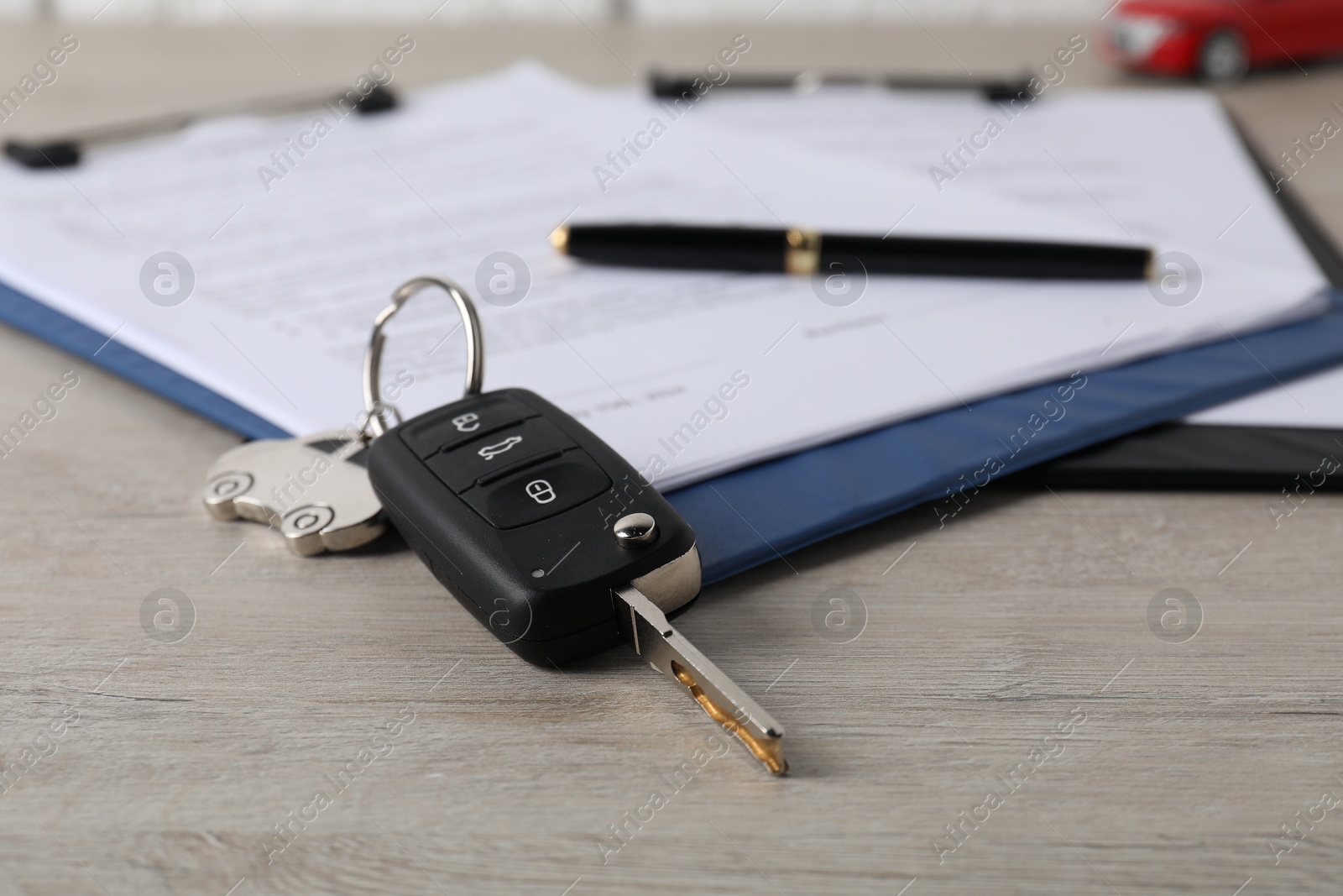 Photo of Car key and purchase agreement on wooden table, closeup. Buying auto