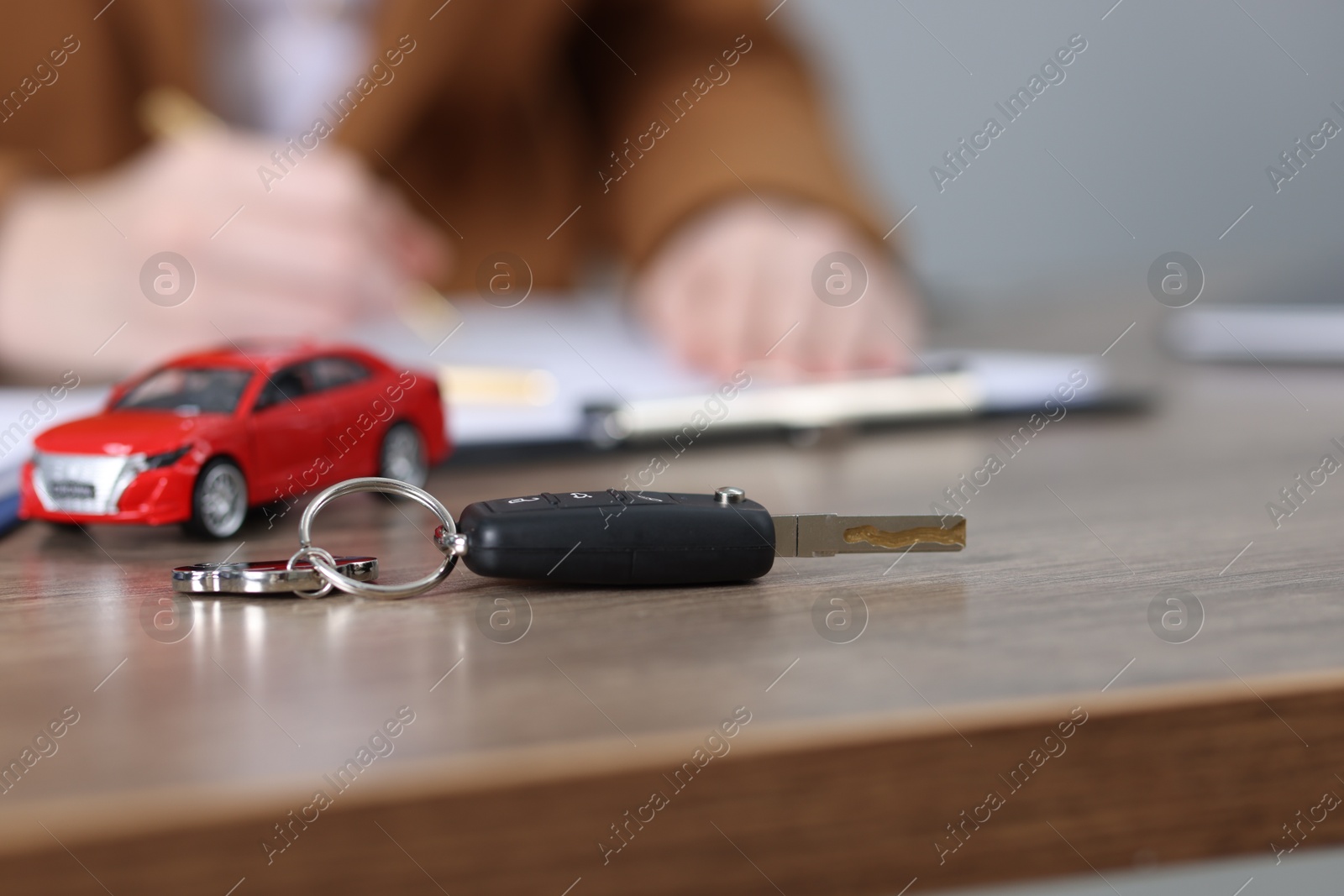 Photo of Car key, model and woman signing purchase agreement at wooden table, selective focus. Buying auto