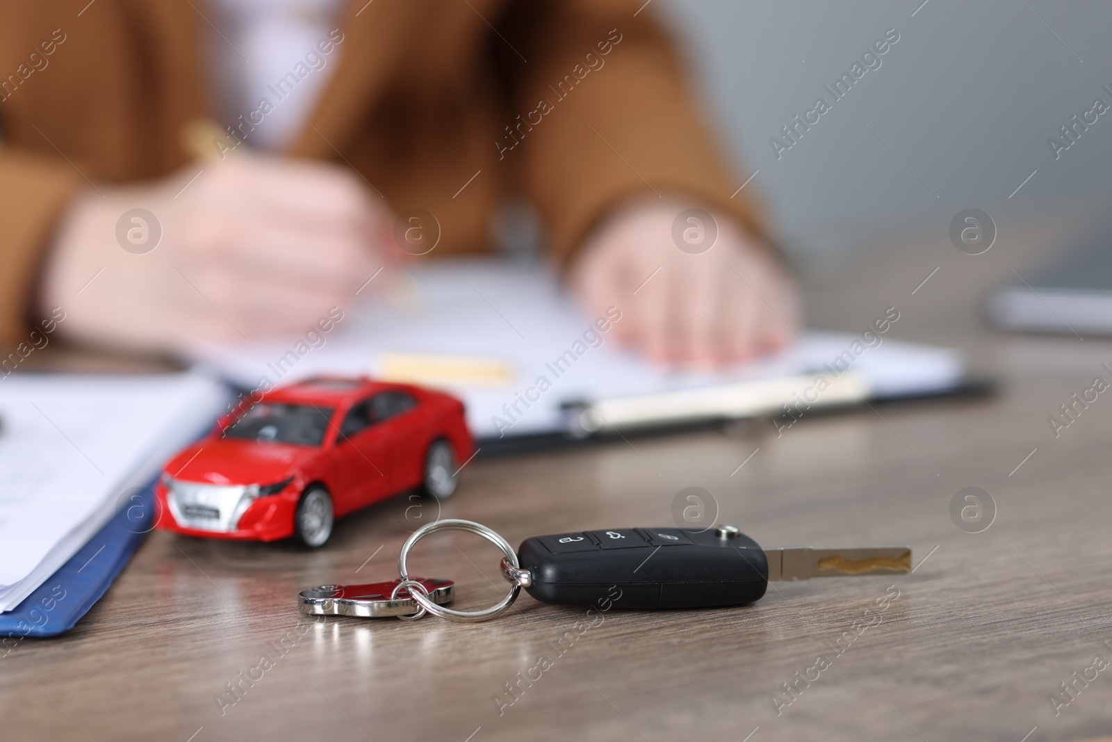 Photo of Car key, model and woman signing purchase agreement at wooden table, selective focus. Buying auto