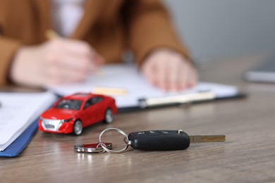 Photo of Car key, model and woman signing purchase agreement at wooden table, selective focus. Buying auto