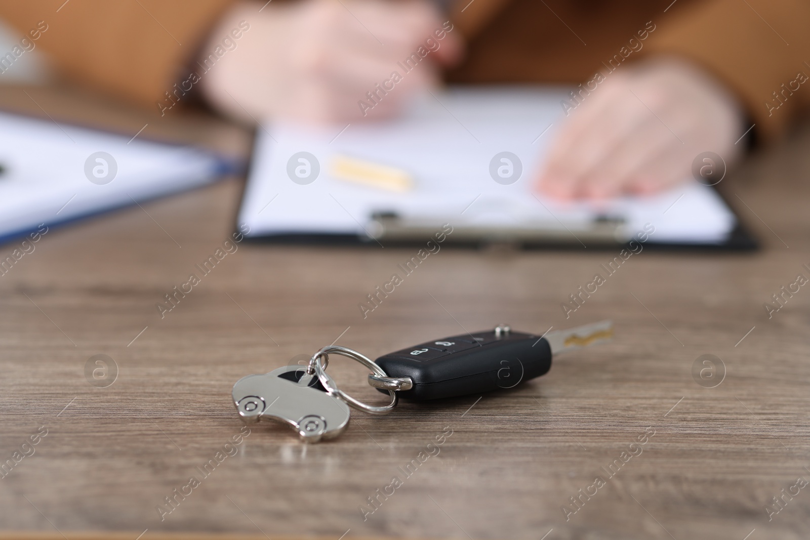 Photo of Car key and woman signing purchase agreement at wooden table, selective focus. Buying auto