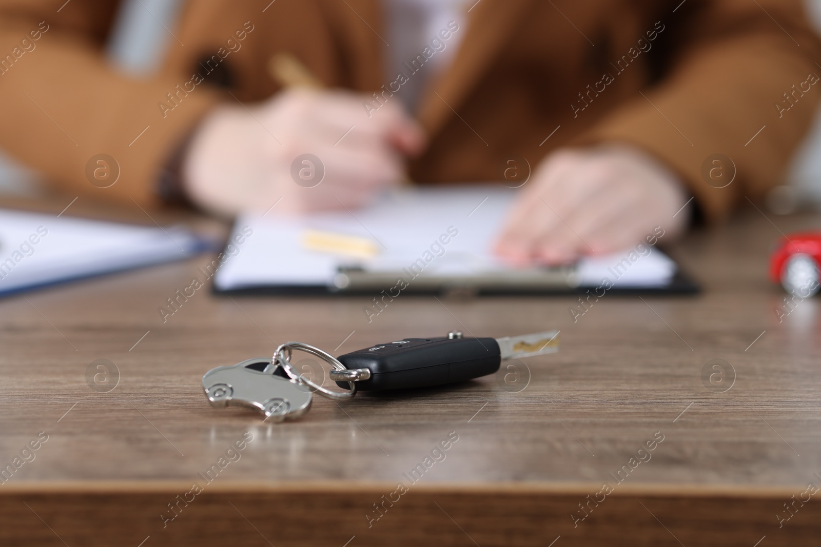 Photo of Car key and woman signing purchase agreement at wooden table, selective focus. Buying auto