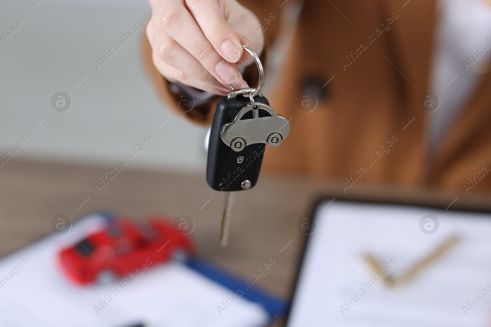 Photo of Dealership agent giving car key to new owner indoors, closeup. Buying auto