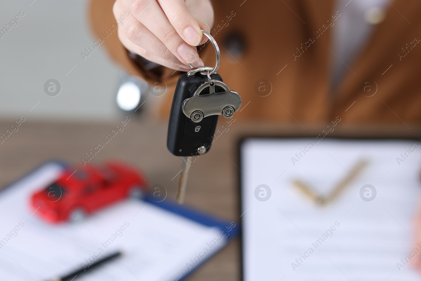 Photo of Dealership agent giving car key to new owner indoors, closeup. Buying auto