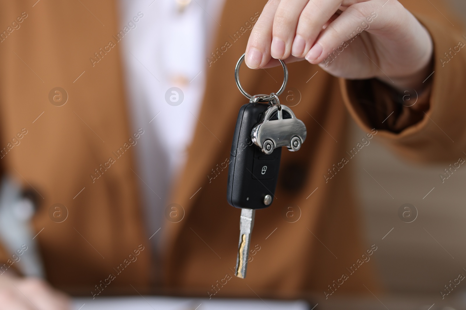 Photo of Dealership agent giving car key to new owner indoors, closeup. Buying auto