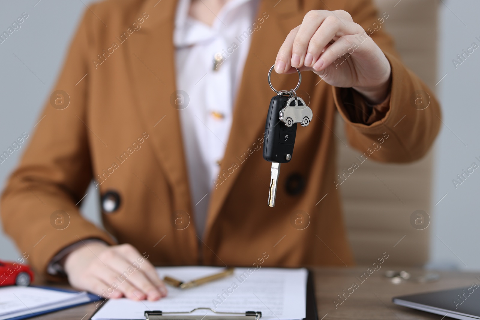 Photo of Dealership agent giving car key to new owner indoors, closeup. Buying auto