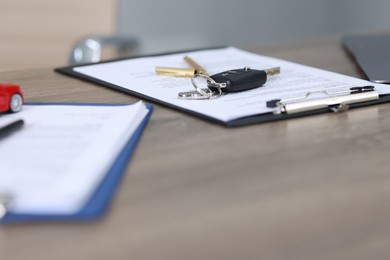 Photo of Car key and purchase agreement on wooden table, selective focus. Buying auto