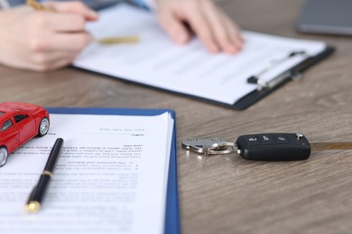 Photo of Car key, model and purchase agreement on wooden table, selective focus. Buying auto