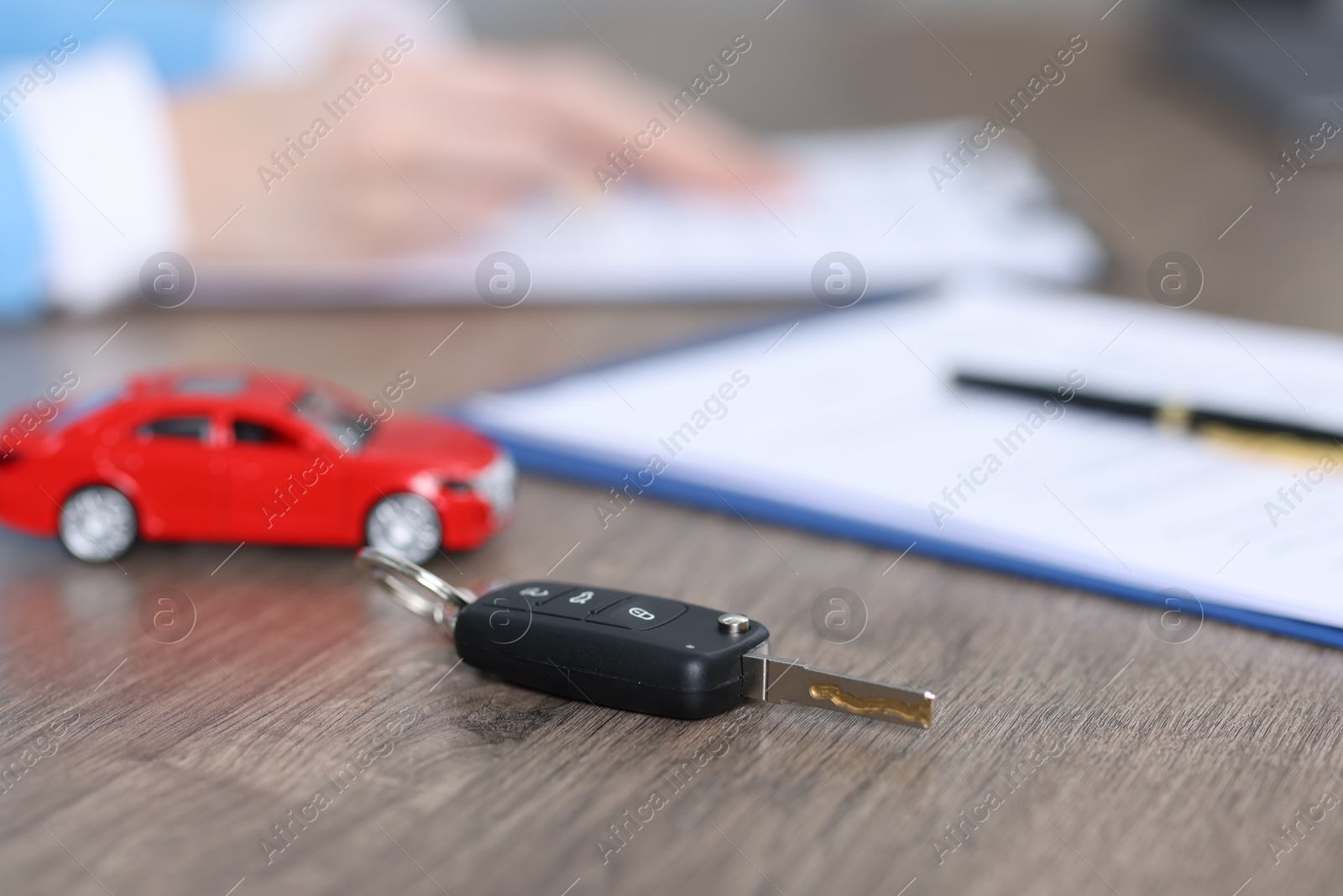 Photo of Car key, model and purchase agreement on wooden table, selective focus. Buying auto