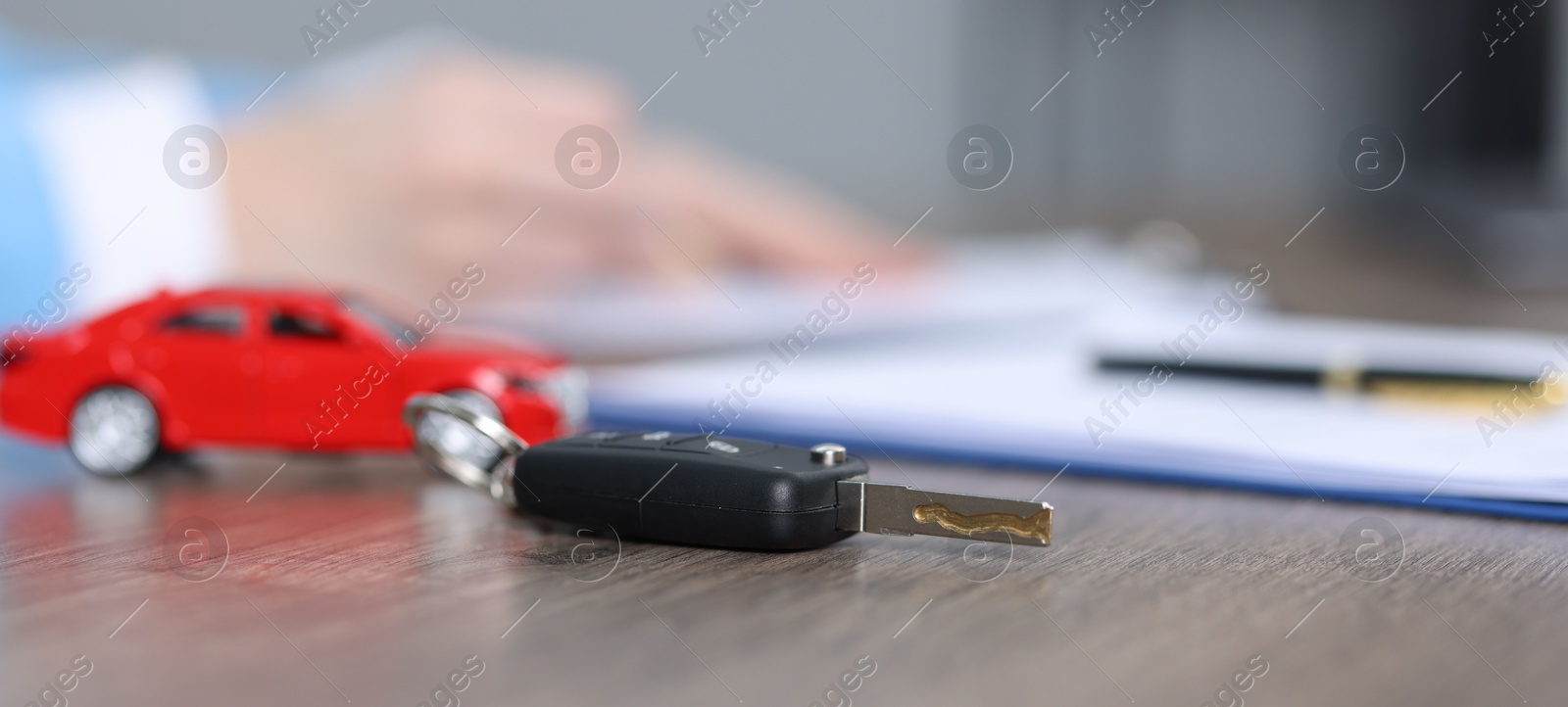 Photo of Car key, model and purchase agreement on wooden table, selective focus. Buying auto