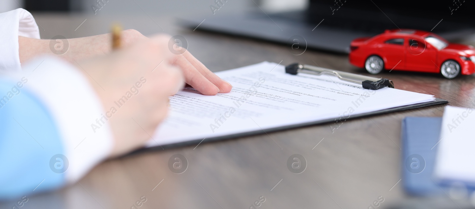 Photo of Woman signing car purchase agreement at wooden table, closeup. Buying auto