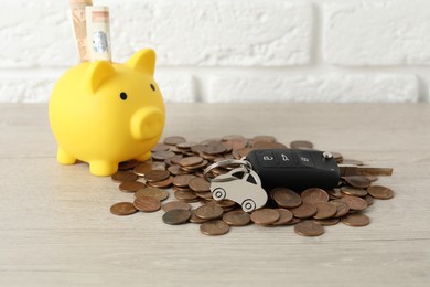 Car key, piggybank and coins on light background