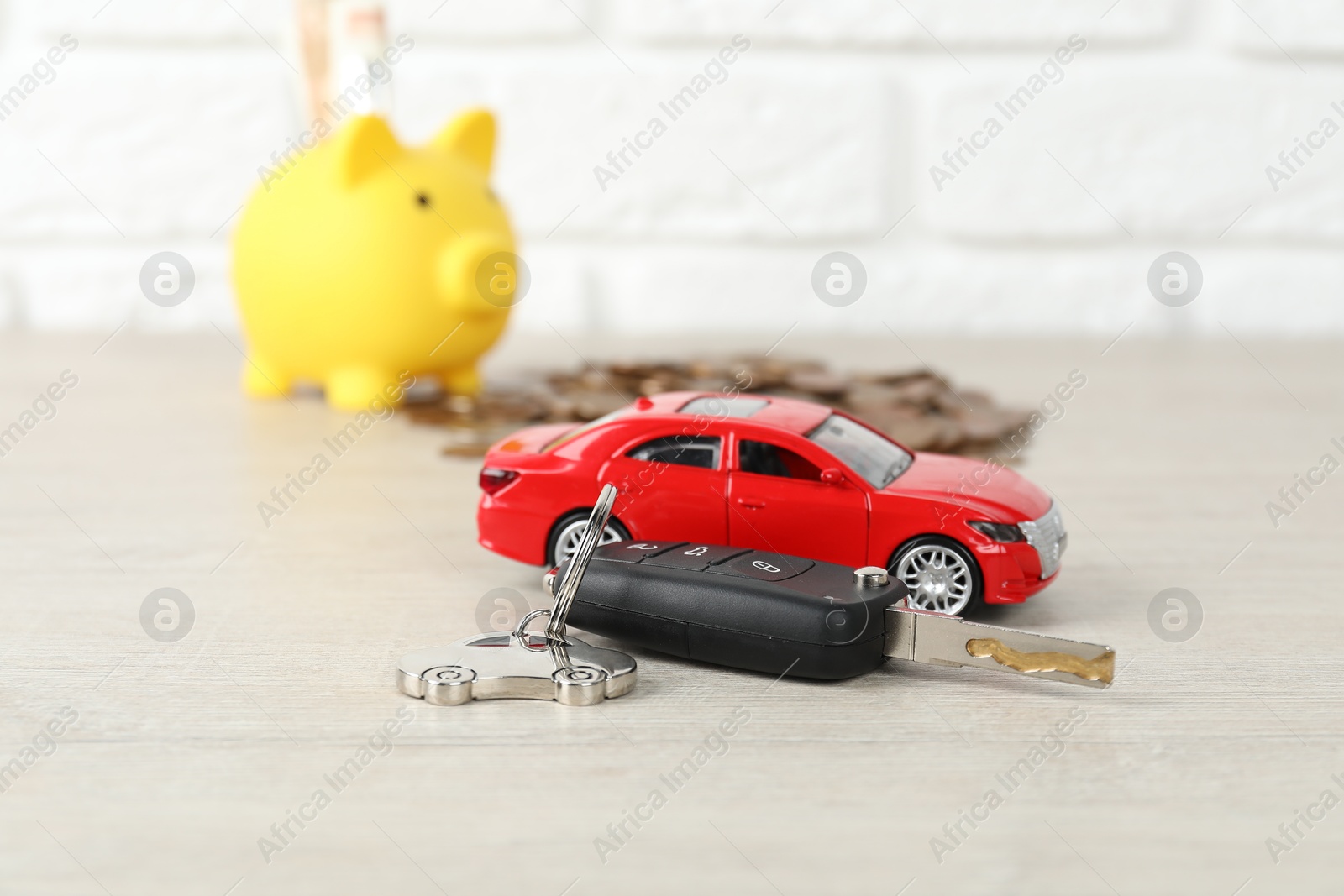 Photo of Car key, model, piggybank and coins on light background, selective focus