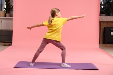 Photo of Cute little girl exercising on fitness mat against pink background