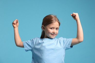 Photo of Cute little girl showing her biceps on light blue background