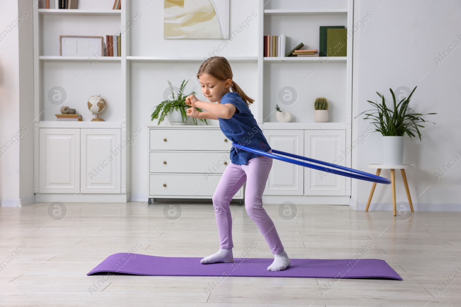 Photo of Cute little girl exercising with hula hoop indoors