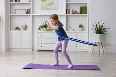 Cute little girl exercising with hula hoop indoors