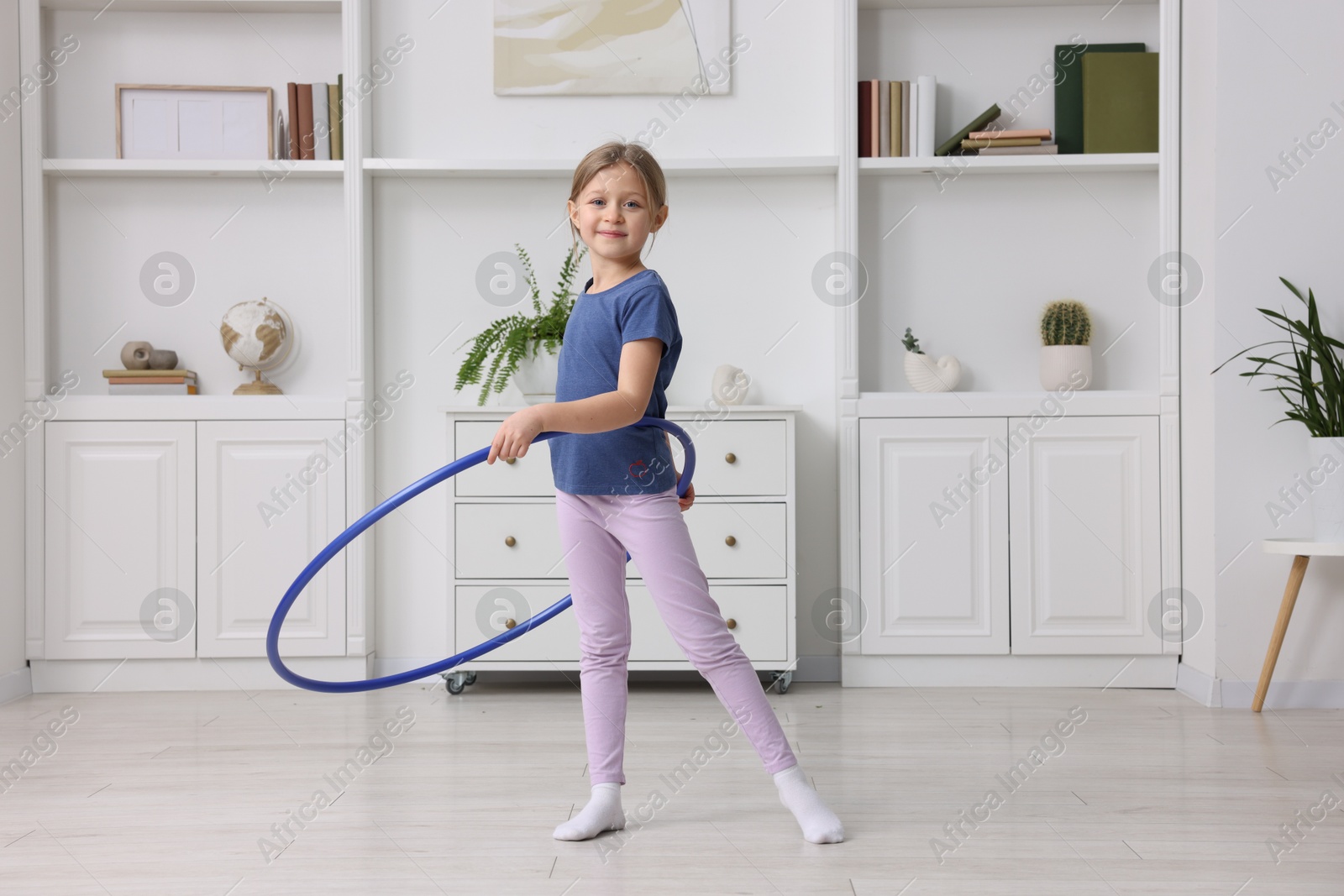 Photo of Cute little girl exercising with hula hoop indoors